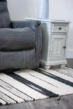 Load image into Gallery viewer, 3x5 rug in varying shades of white, grey, and black stripes in a modern living room with a reclining chair and side table. 