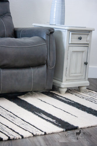 3x5 rug in varying shades of white, grey, and black stripes in a modern living room with a reclining chair and side table. 